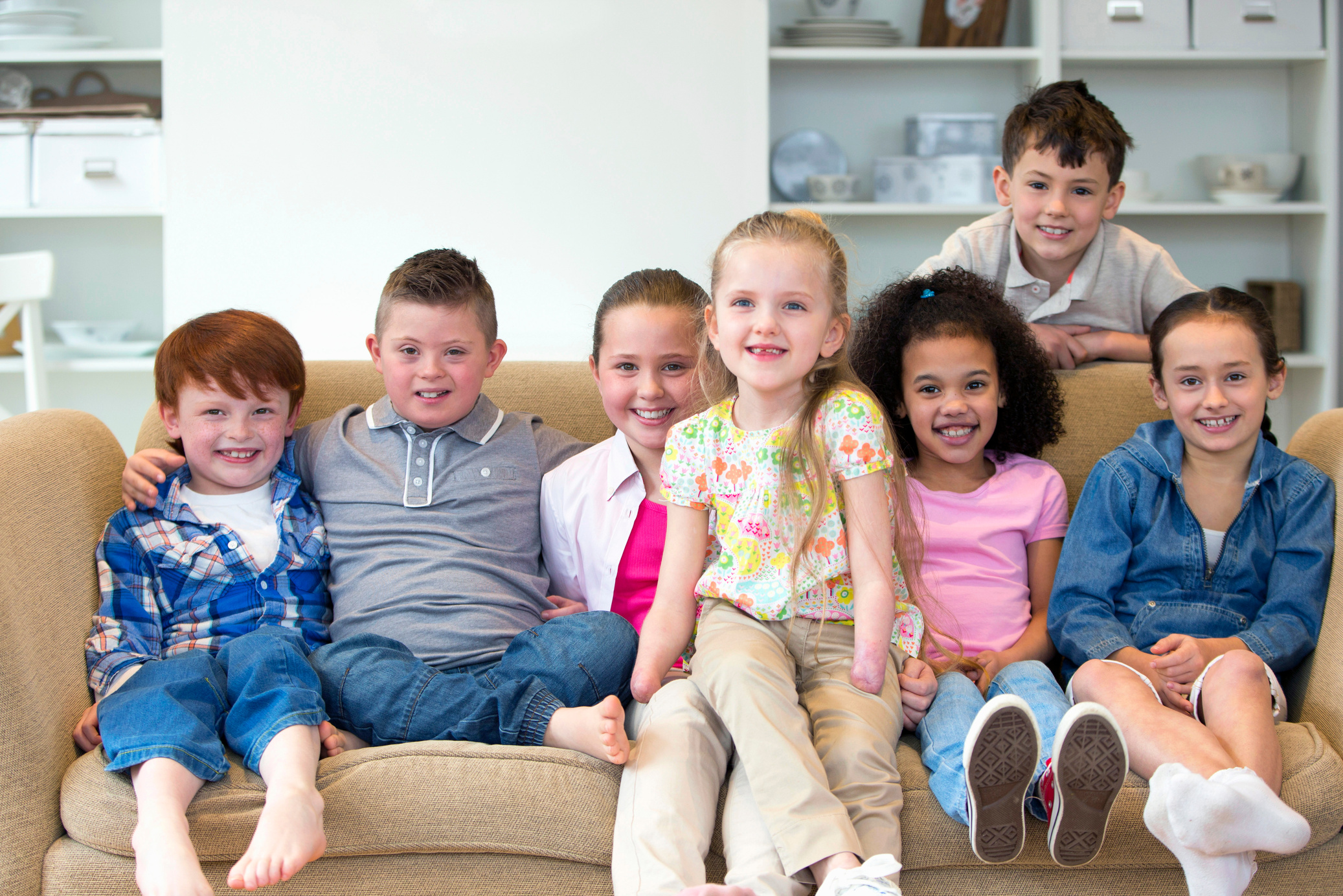 Portrait Of Disabled Children Sitting On Sofa With Friends